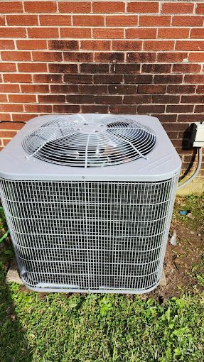 A large air conditioner is sitting in front of a brick wall.