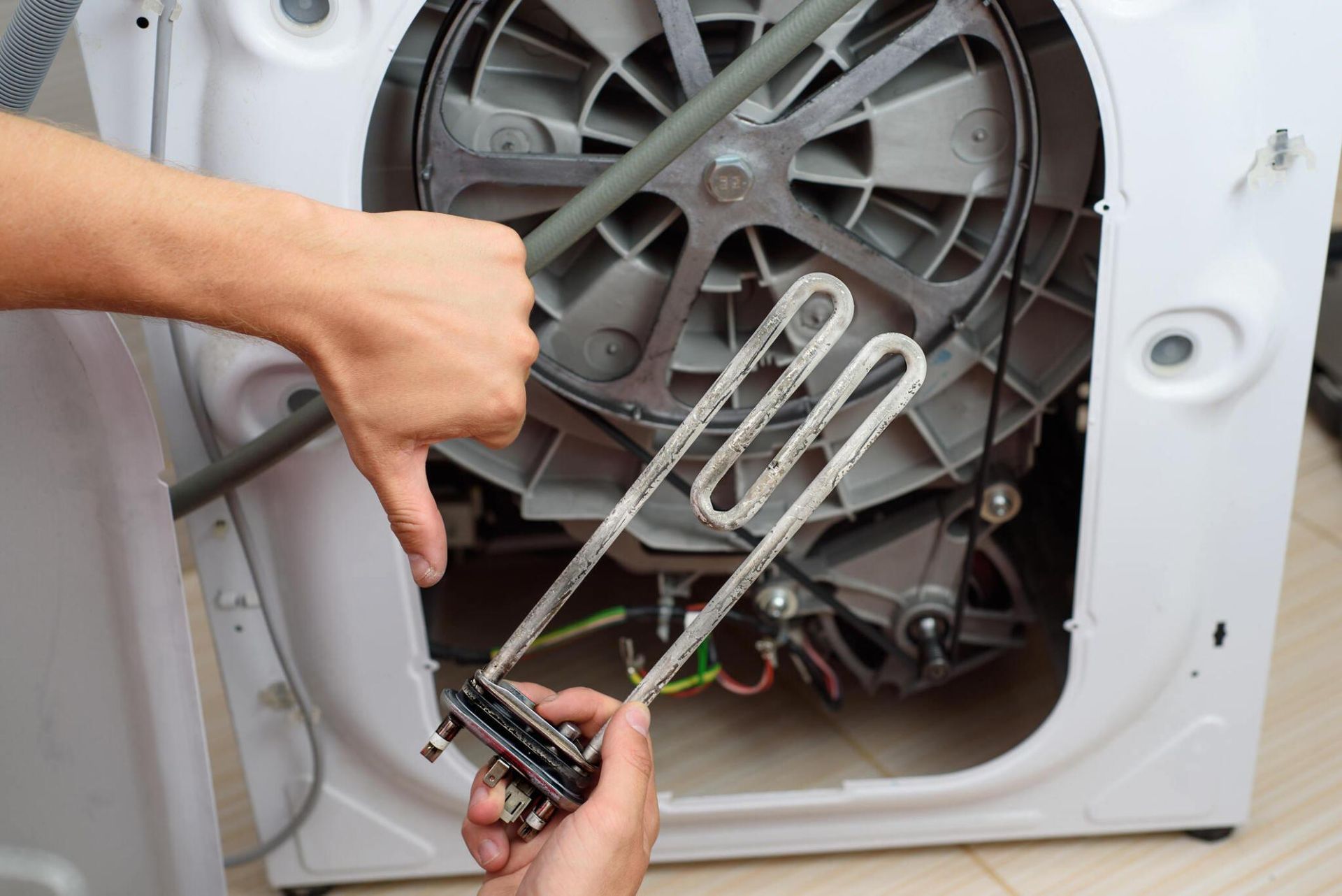 A person is fixing a washing machine with a wrench.