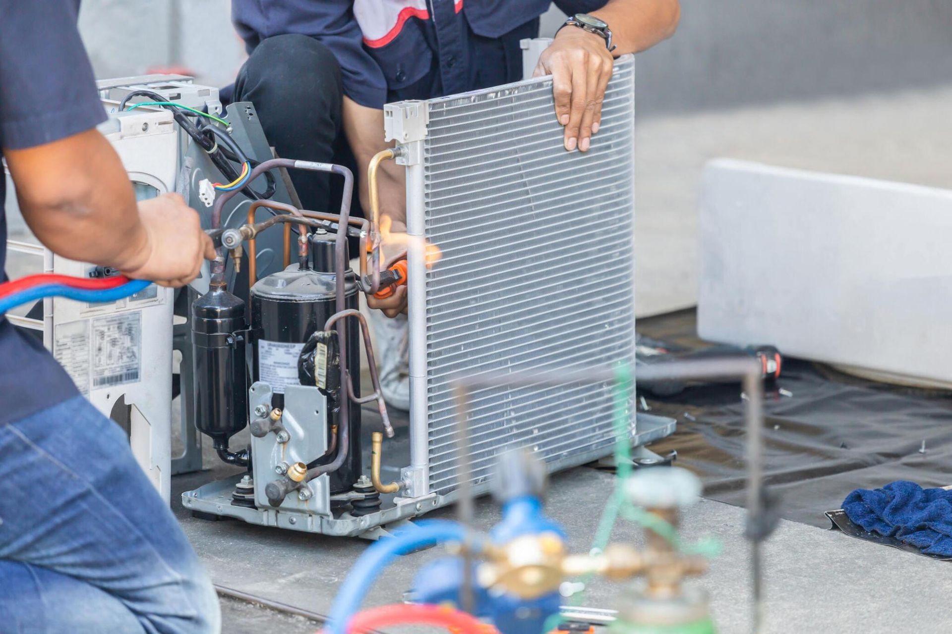 A couple of men are working on an air conditioner.