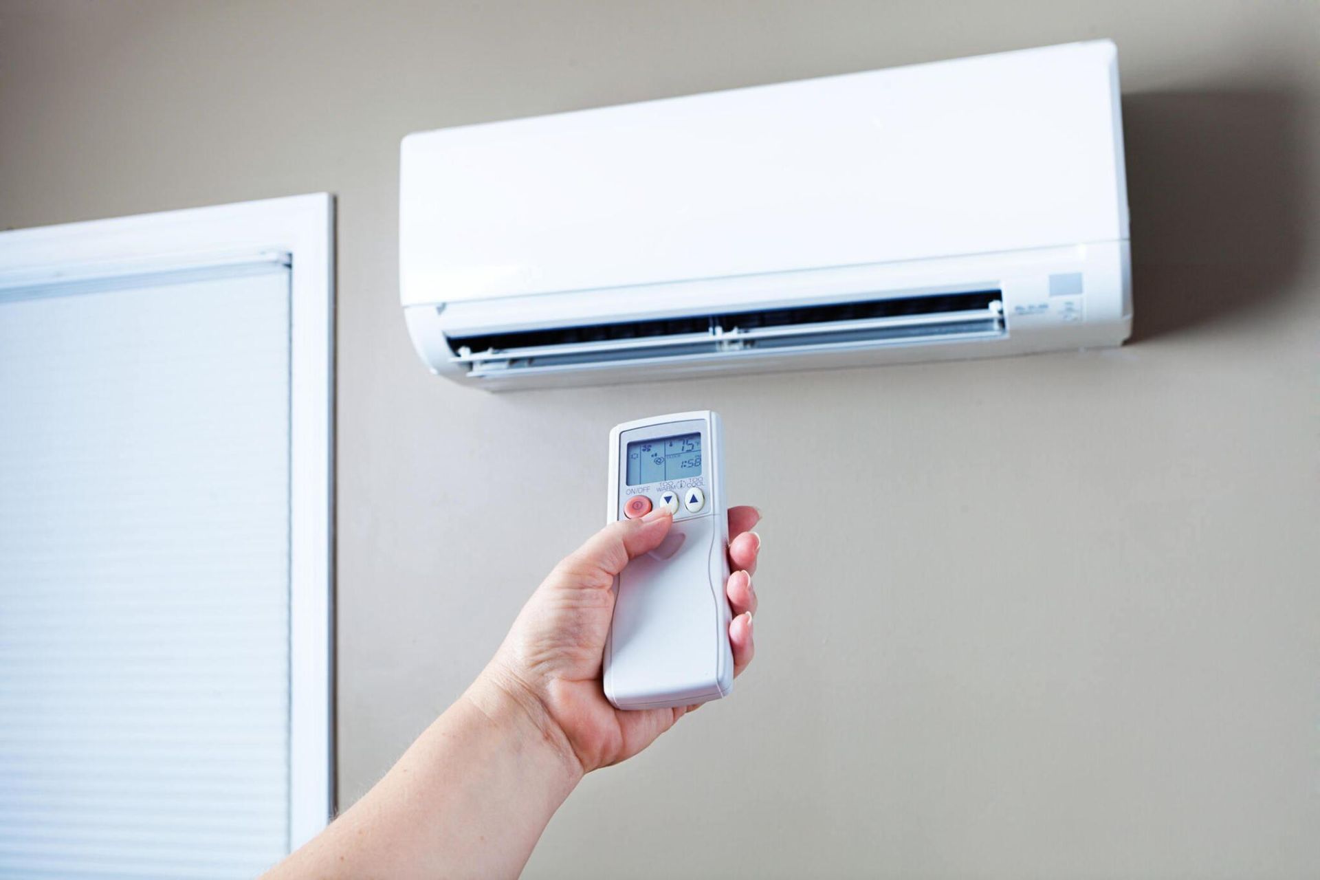 A person is holding a remote control in front of an air conditioner.