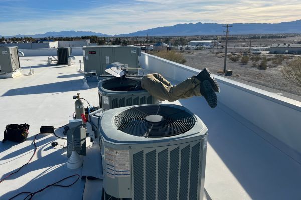 Technician adjusting pipes under a wall-mounted boiler with a wrench, surrounded by red insulated plumbing lines.