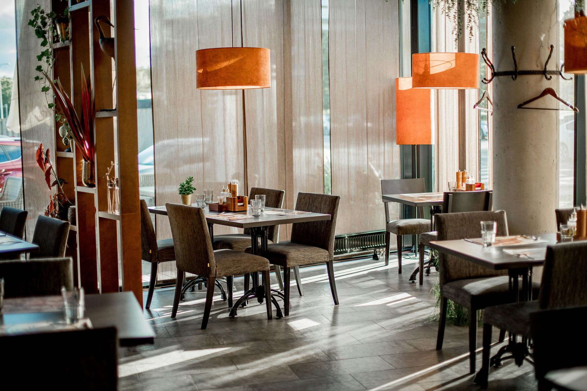 Modern restaurant dining area with tables, chairs, and orange pendant lamps near tall windows
