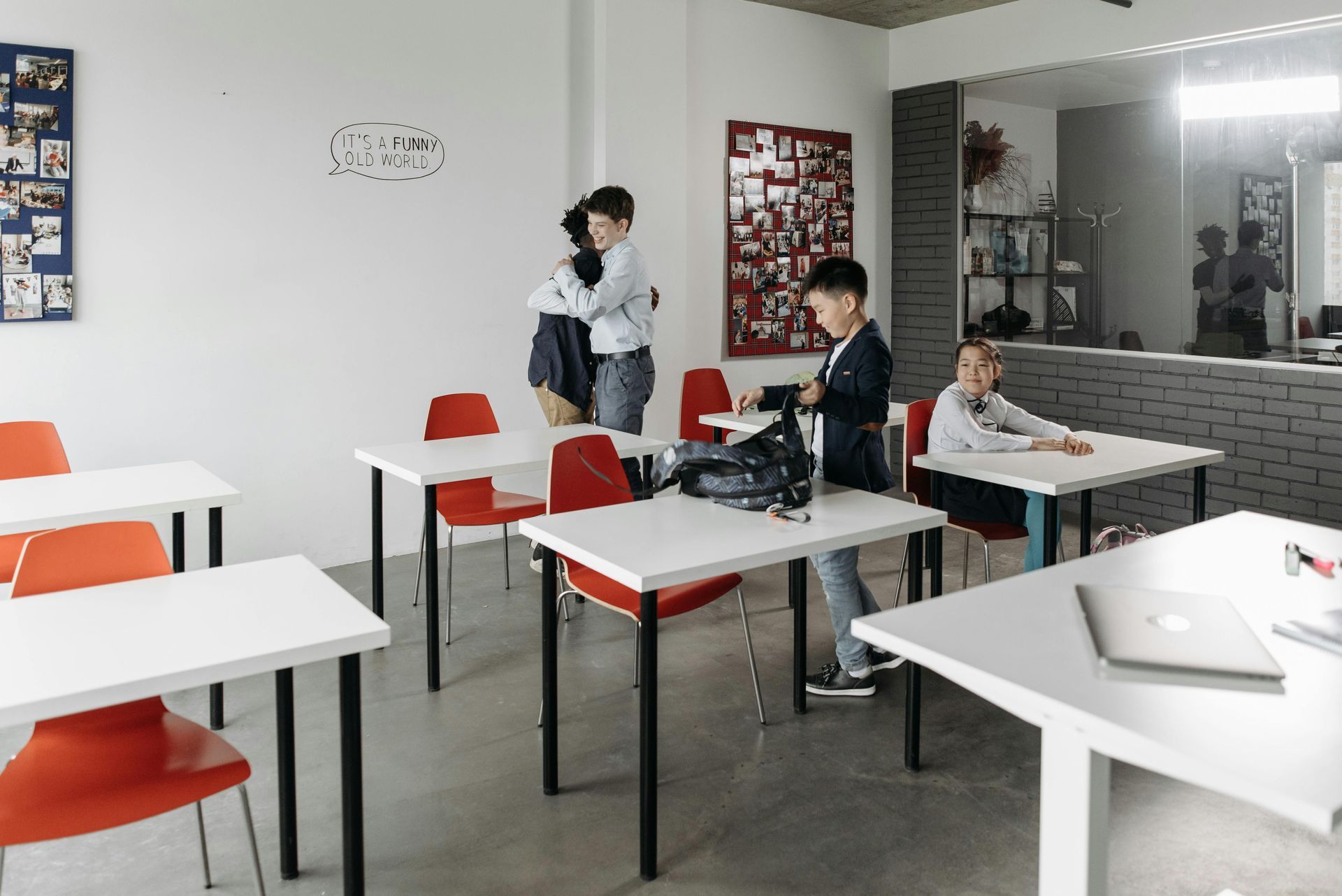 Classroom with orange chairs, white tables, and three people talking near the back wall.
