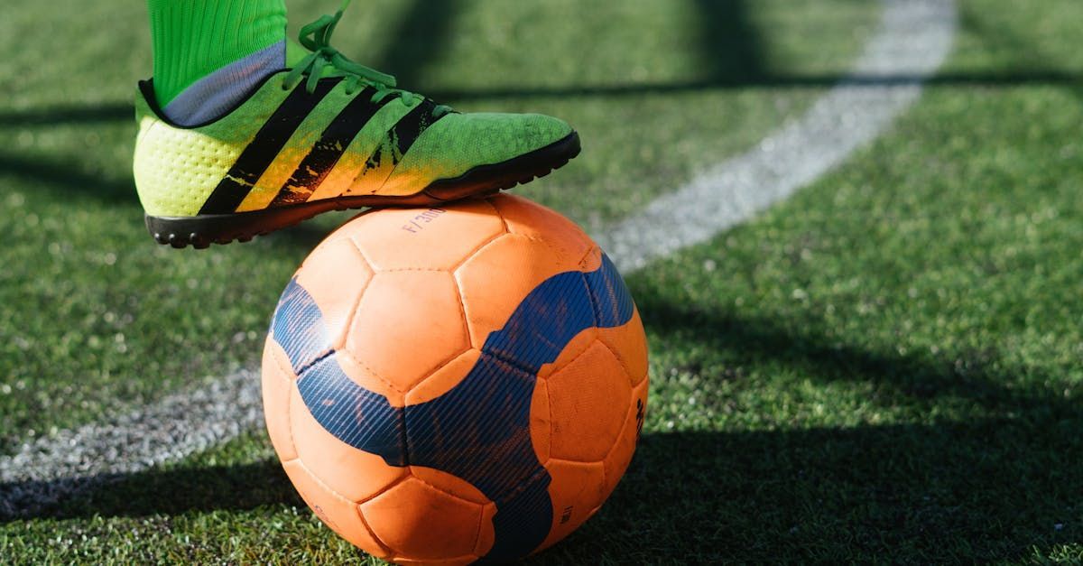 Orange soccer ball on a field with a green cleated shoe nearby