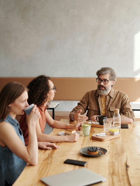 A group of people are sitting around a wooden table having a meeting.