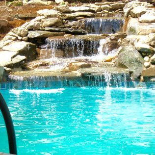 A tiered stone waterfall cascading into a bright blue swimming pool.