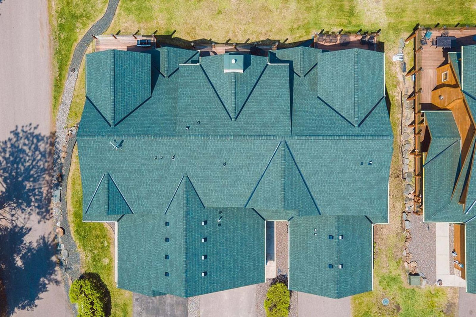Overhead view of a teal-roofed house complex in a grassy area with a road and wooden decks.