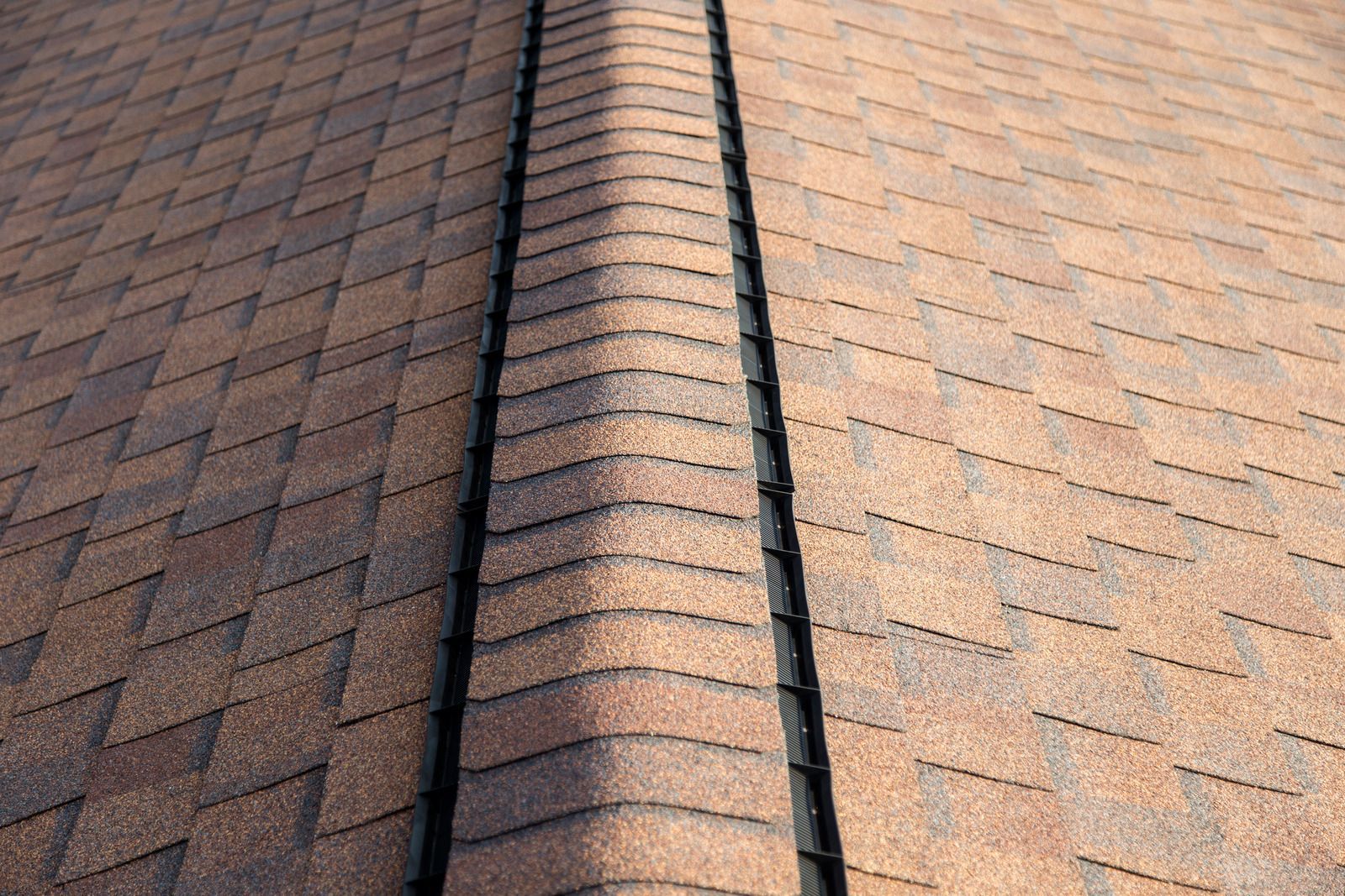 Close-up view of a brown shingled roof with a dark line where two roof sections meet.