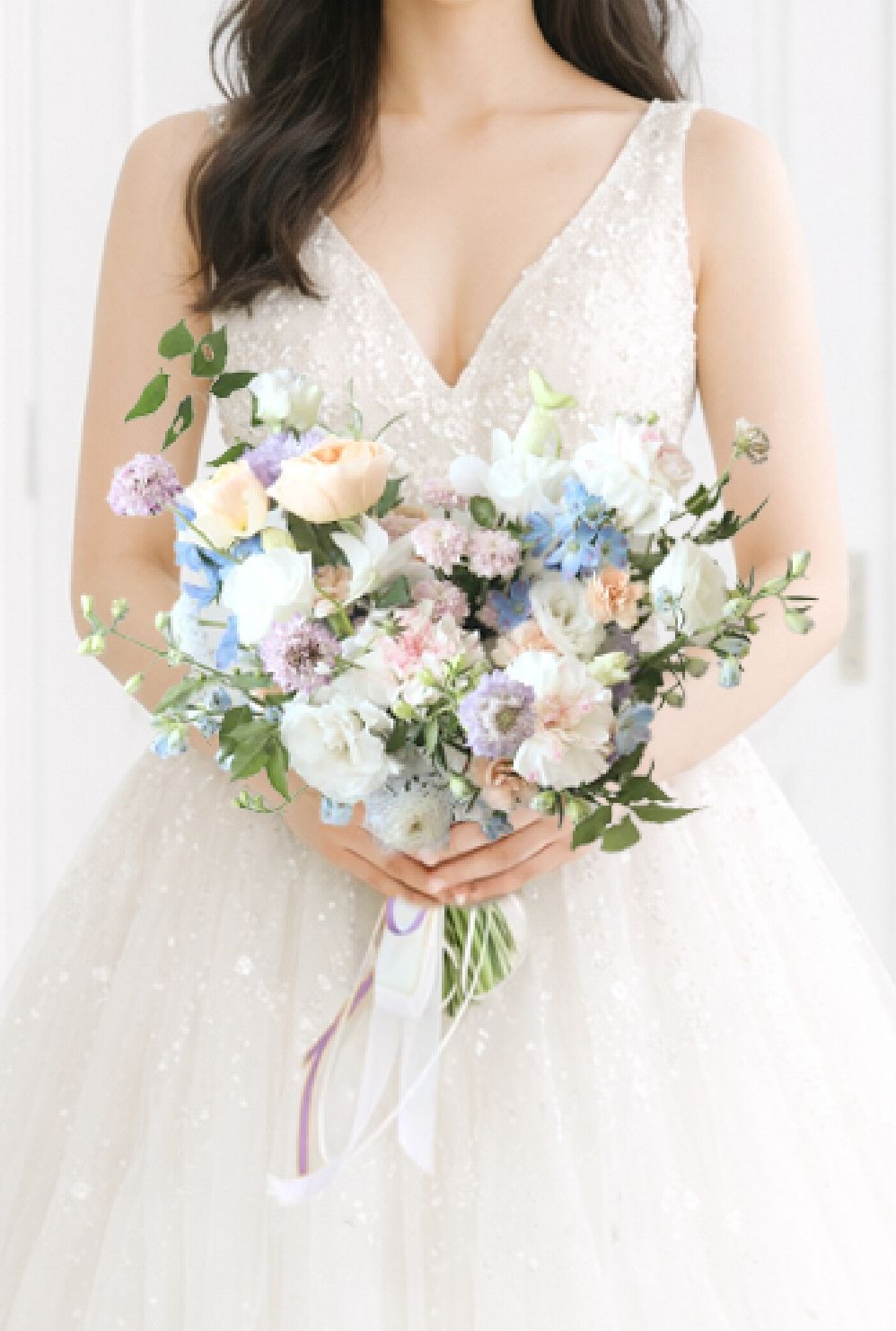 身穿白色蕾絲婚紗的新娘手捧一束淡粉色野花花束
