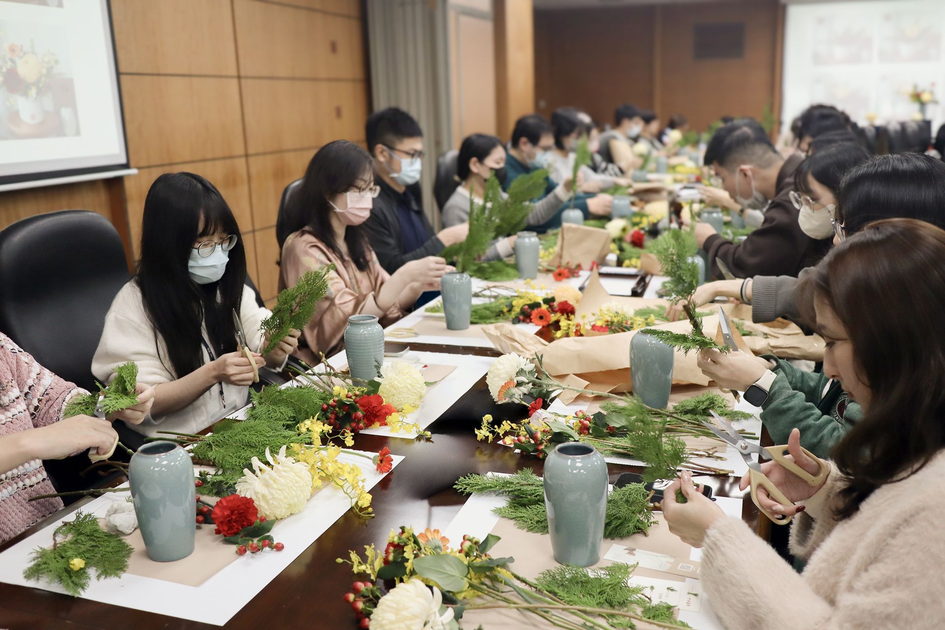 在工作室裡，人們圍坐在長桌旁，擺弄著鮮花和綠植。