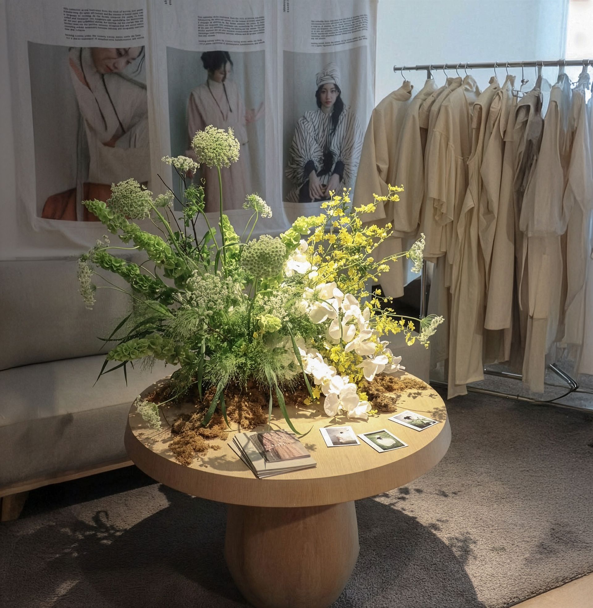 精品店櫥窗展示著米色服裝架、圓形木桌和鬱鬱蔥蔥的綠色花卉擺設。