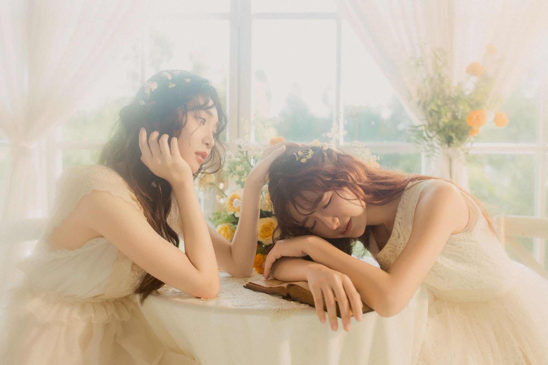 兩名身穿白色洋裝的女子在陽光照耀下的窗邊桌旁休息，背景是柔和的花朵。