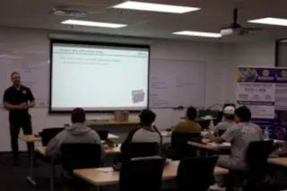 Classroom training session with instructor presenting at a projector screen and several attendees seated at desks