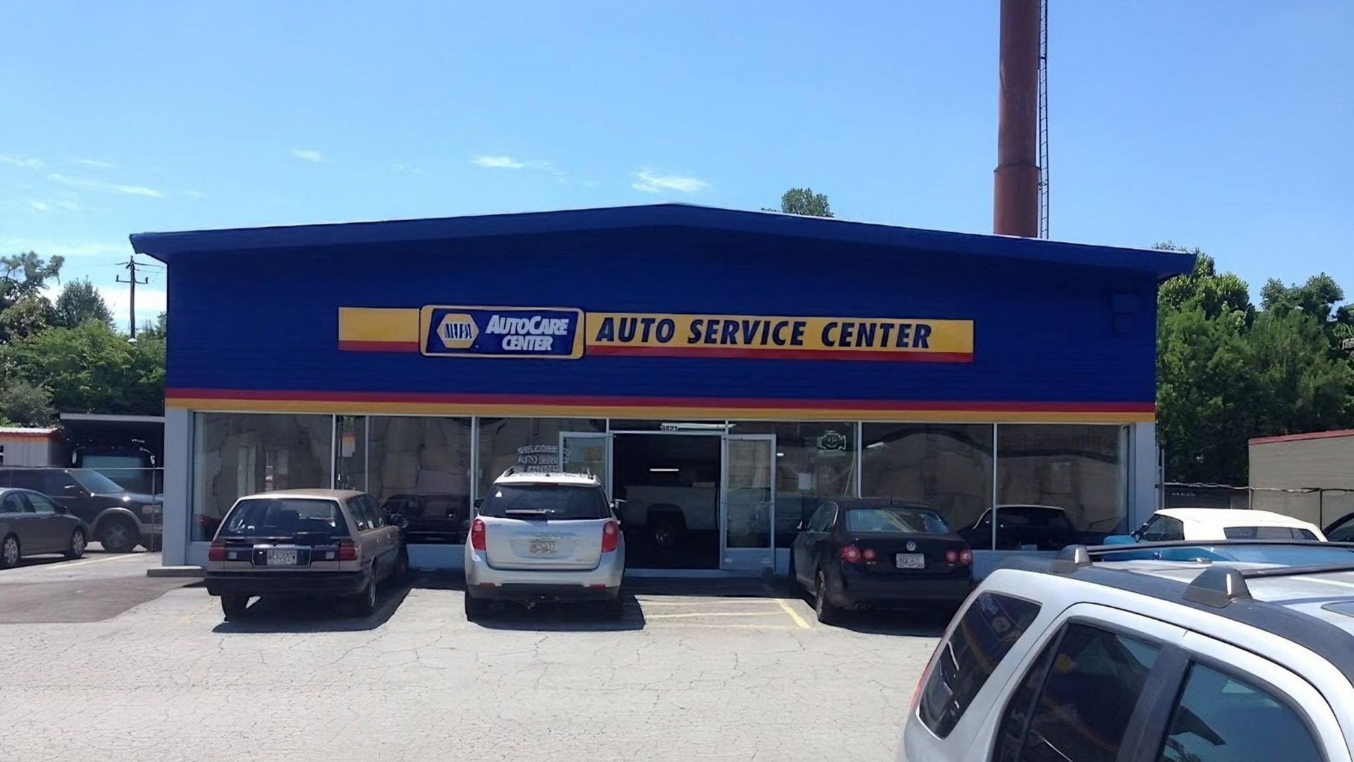 Auto service center storefront with several parked cars under a clear blue sky