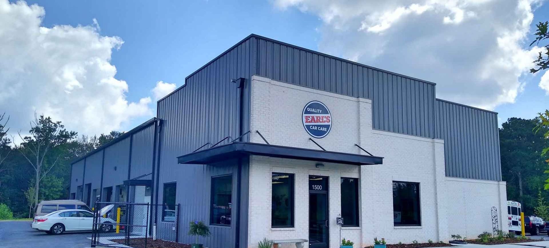 Industrial building with white and gray siding, storefront entrance, and parked car under a partly cloudy sky