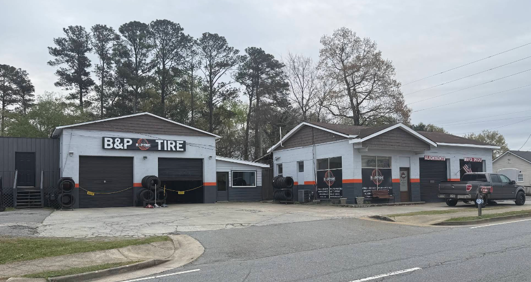 Auto repair shop building with cars parked outside and a roadside sign under cloudy skies