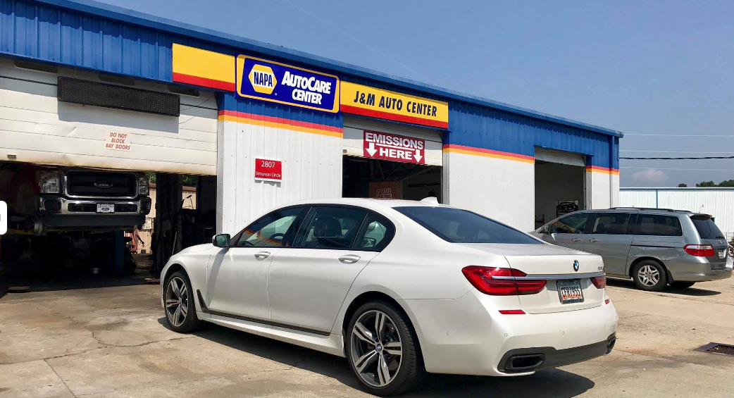 White BMW parked outside an auto repair shop with blue roof and open garage bay
