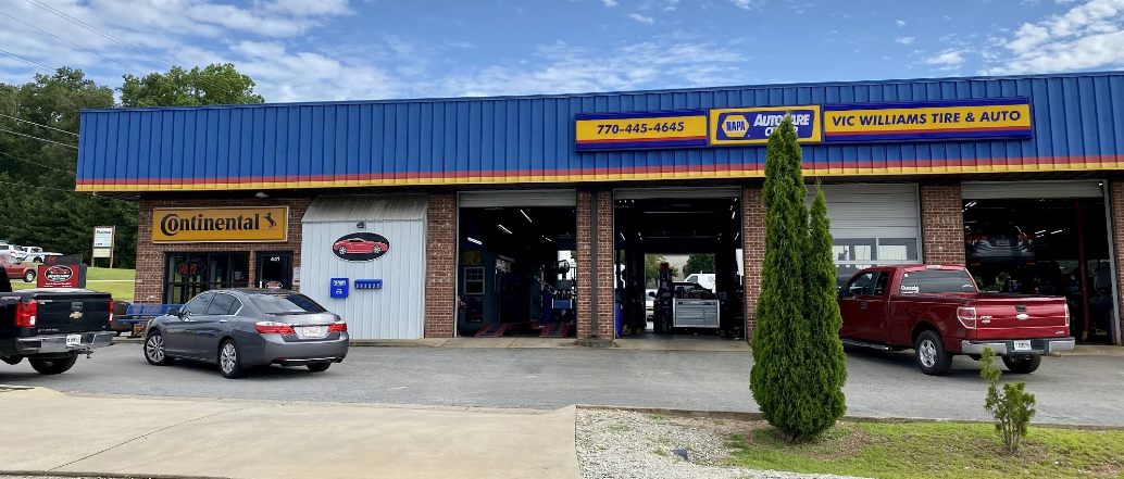 Auto shop storefront with blue roof, open garage bays, and parked vehicles in front