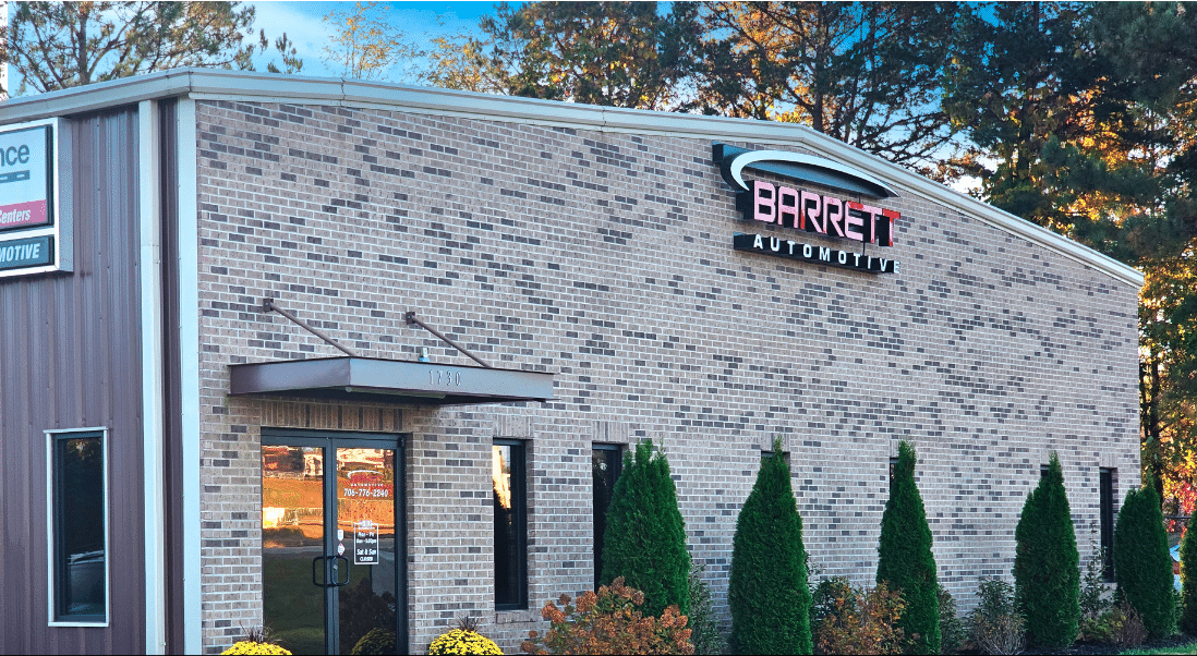 Stone-front commercial building with a red sign and tall green shrubs at the entrance