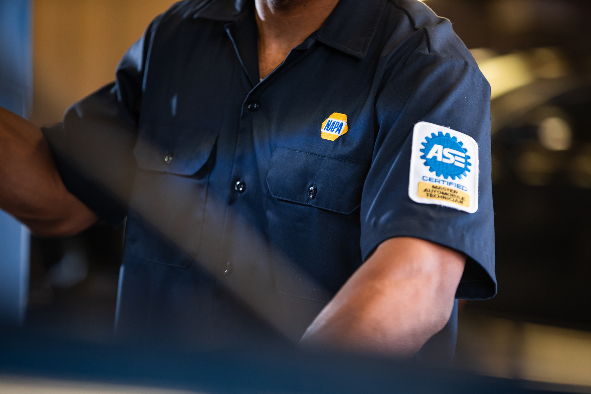 Person in dark blue work shirt with logo patches, seated indoors at a desk.