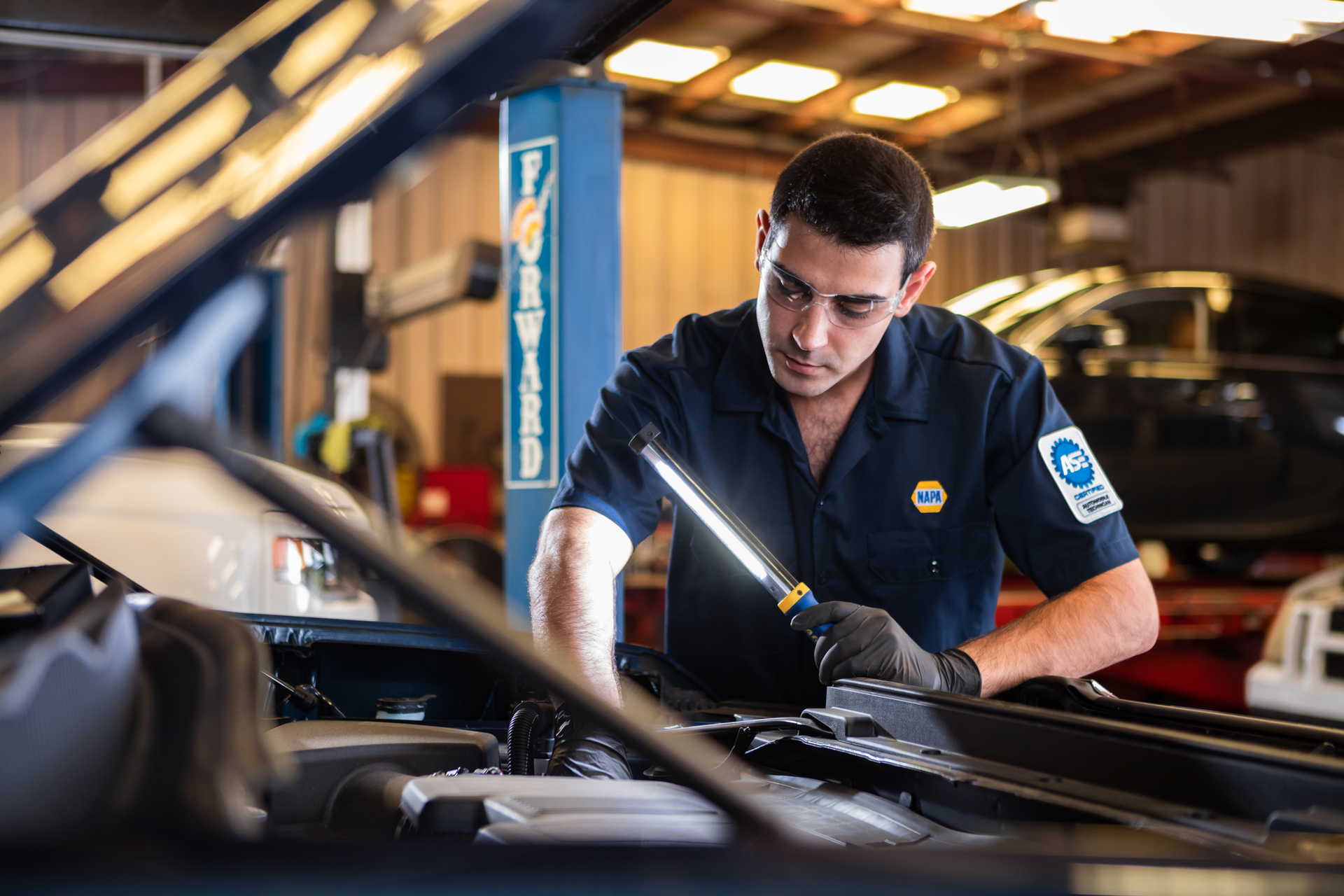 Mechanic inspecting a car engine with a flashlight in a garage workshop