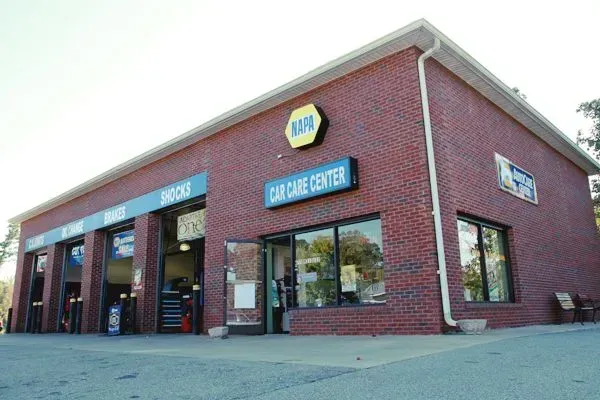 Brick auto repair shop with blue signs and open service bays under a cloudy sky