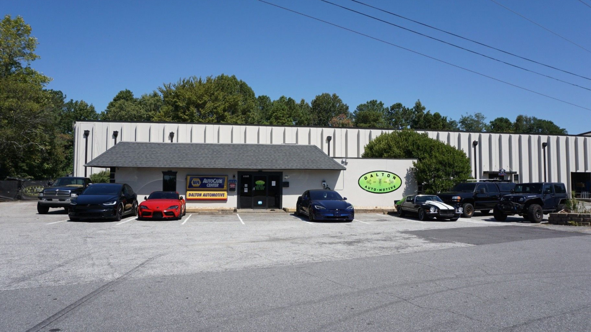Low building with storefronts and parked cars in front, under a clear blue sky