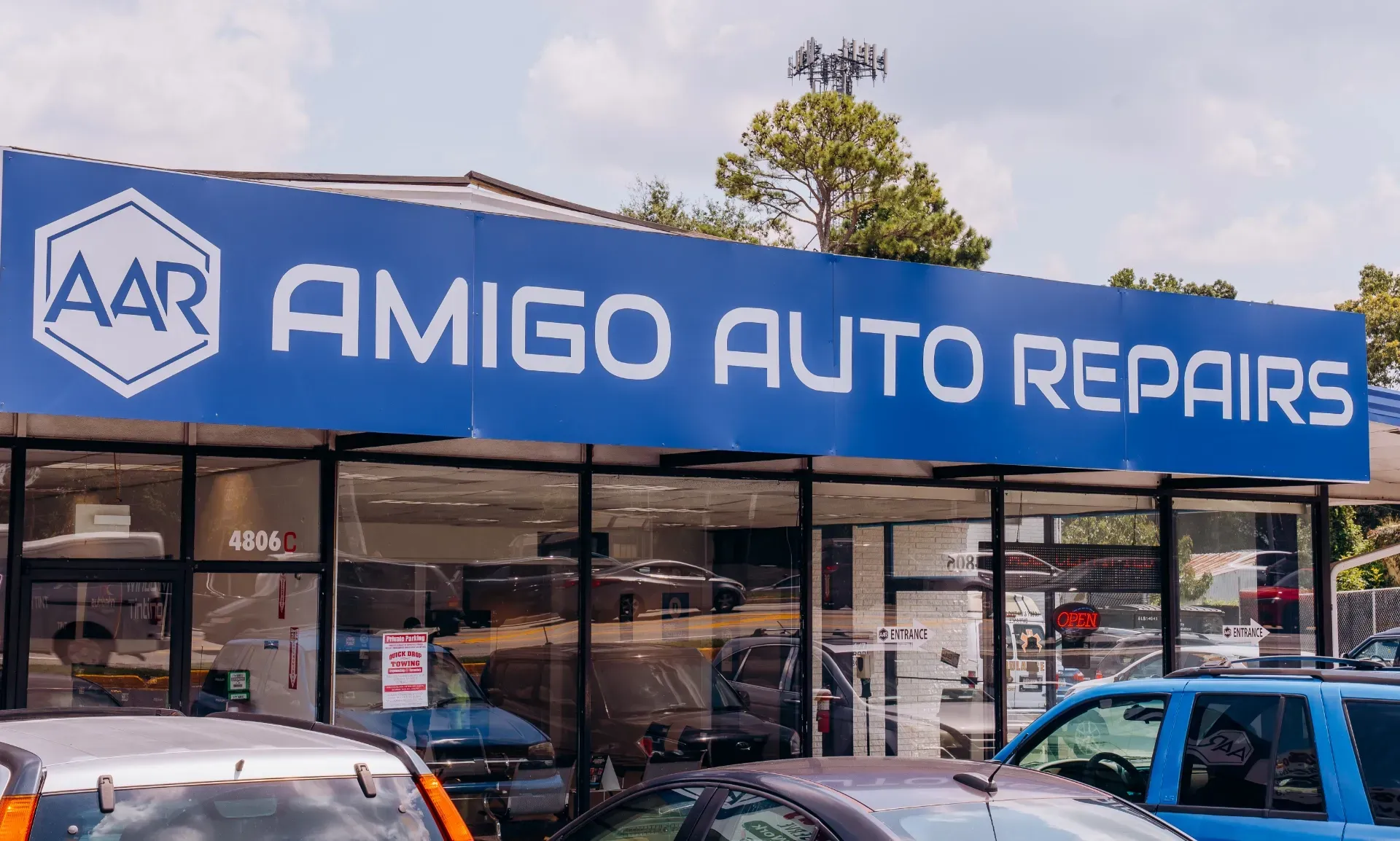 Blue AMIGO AUTO REPAIRS storefront with parked cars outside