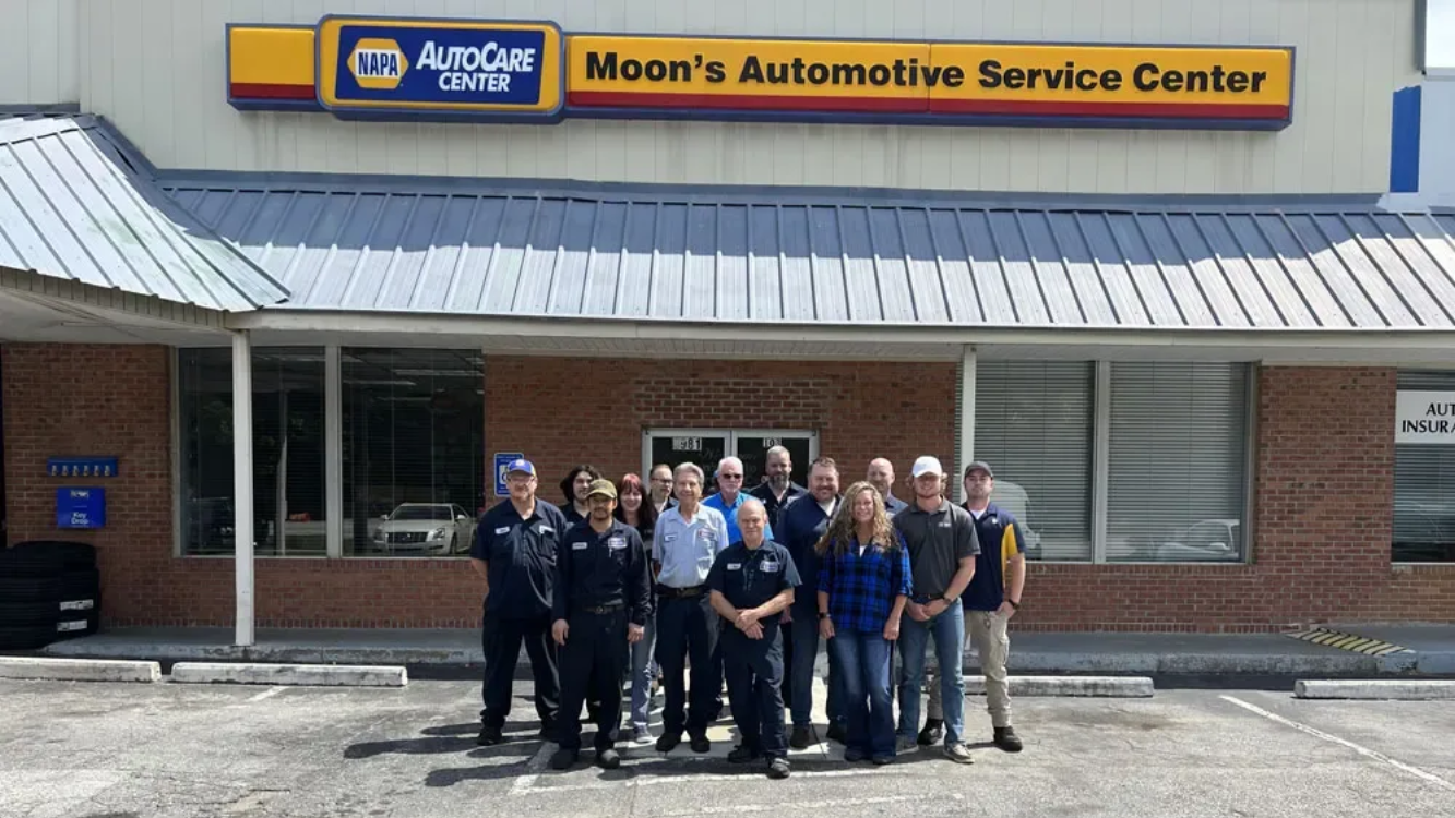 Group of employees posing outside Moon's Automotive Service Center storefront.