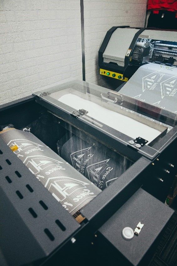 A DTF printer in operation, showing a printed roll of film being processed in a professional studio setting.