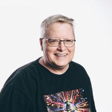 Smiling older man with glasses wearing a black graphic t-shirt against a white backdrop.