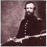 Man in dark military uniform holding a saber. Brown-toned studio portrait.