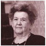 a black and white photo of an elderly woman standing in front of a wall .