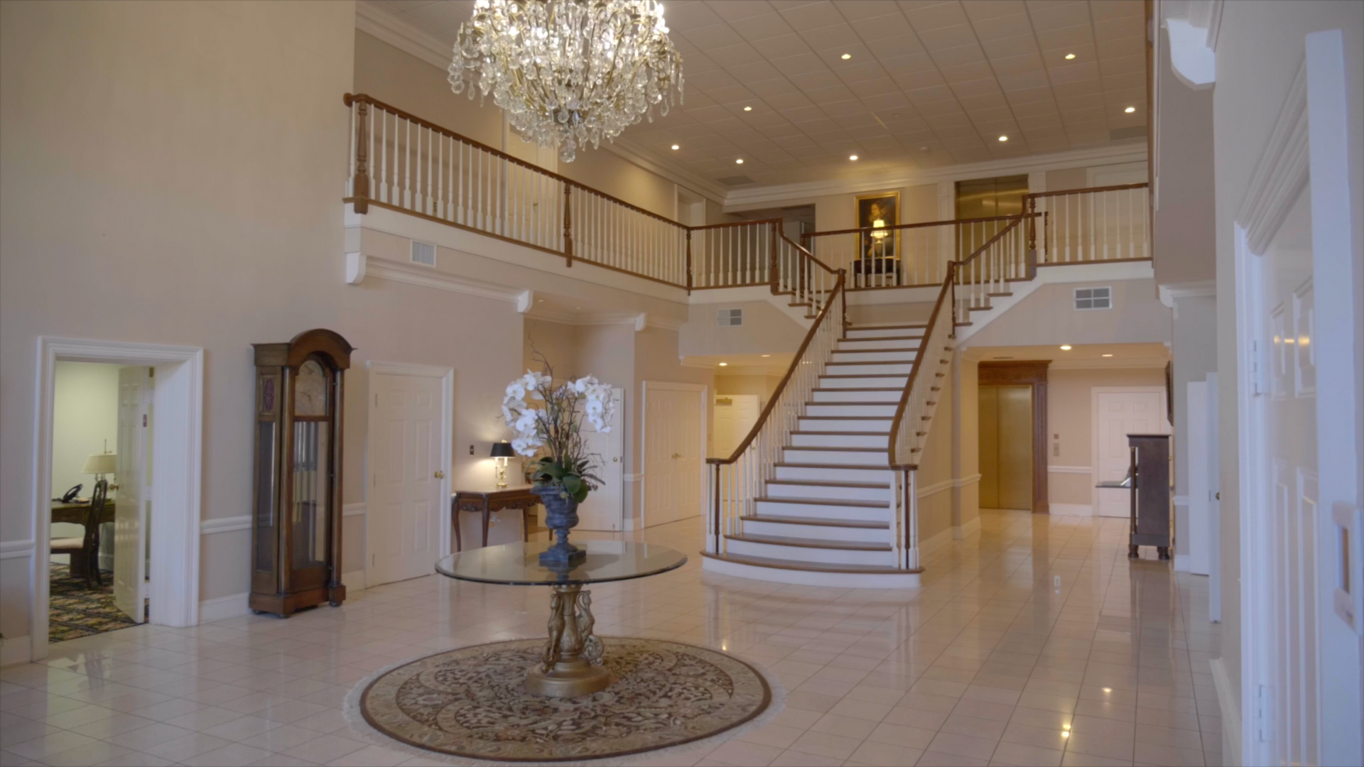 Spacious, opulent entry hall with grand staircase, crystal chandelier, and marble floors.