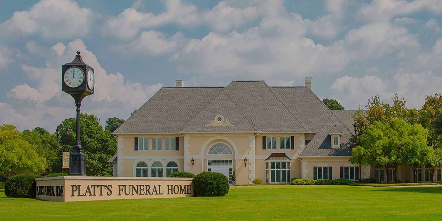 Platt's Funeral Home, a beige building with a clock tower in front, on a green lawn under a blue sky.