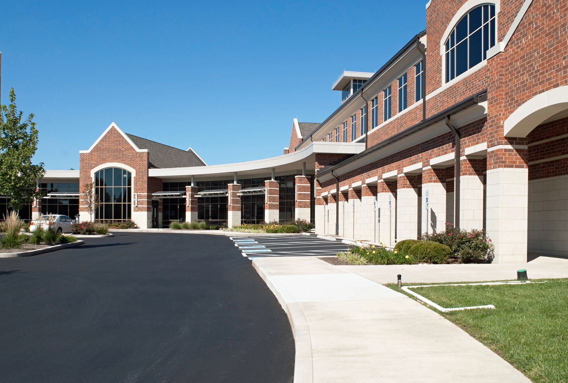 Red brick building with arches, curved entrance, and black asphalt drive on a sunny day.