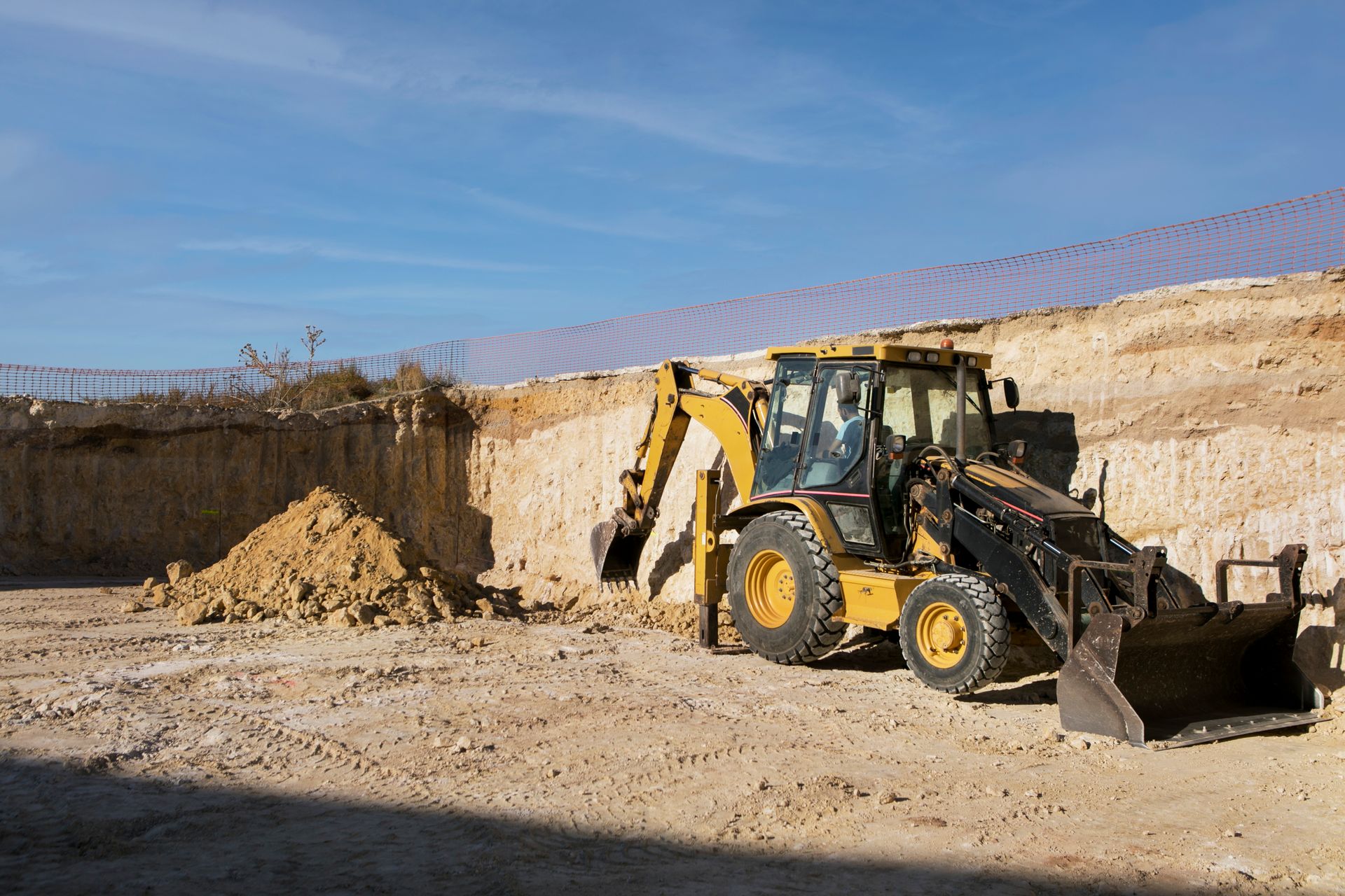 Yellow backhoe parked near a dirt pile at a construction site against a blue sky.