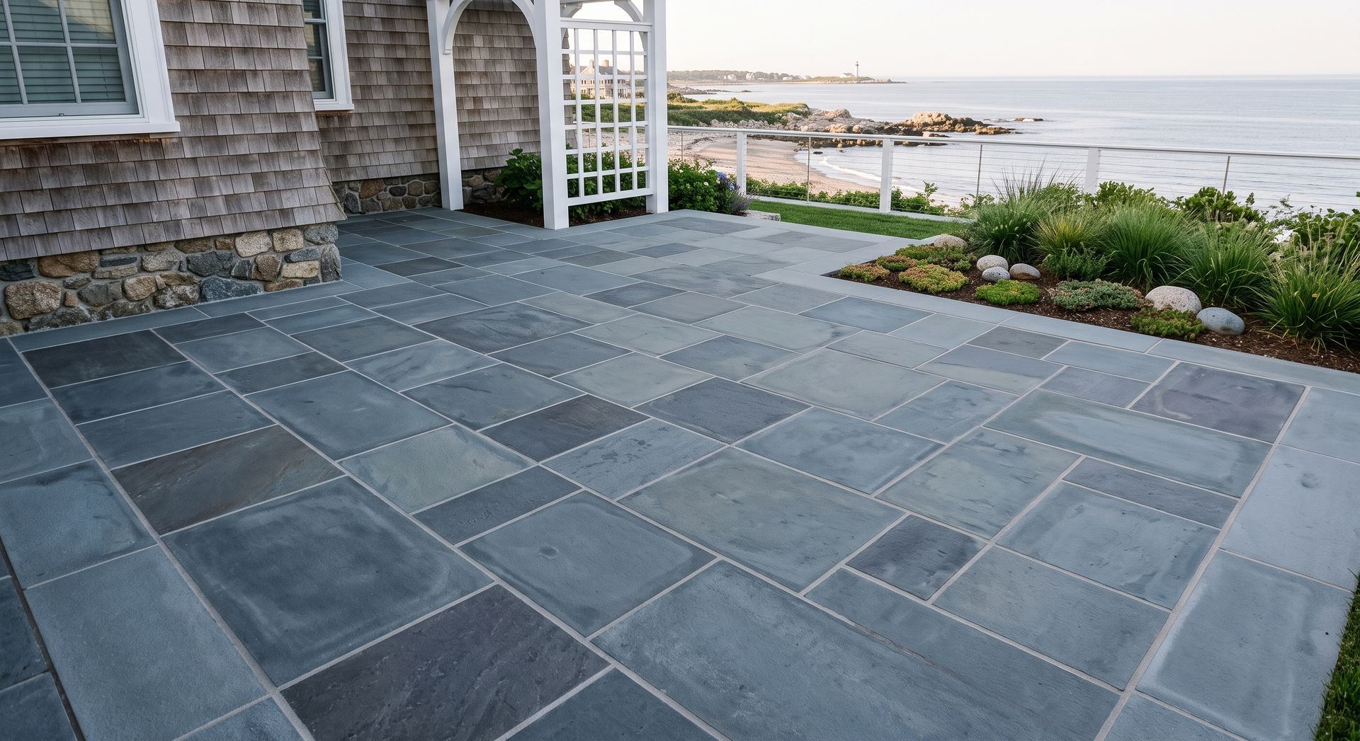 A clean, geometric view of a premium bluestone patio featuring crisp, clear joints and immaculate stone borders near a coastal home.
