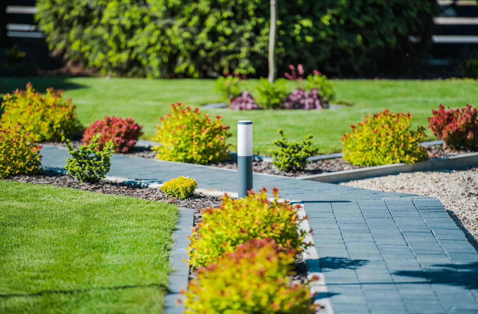 Well-manicured yard with stone path, green lawn, colorful shrubs, and modern light fixtures.