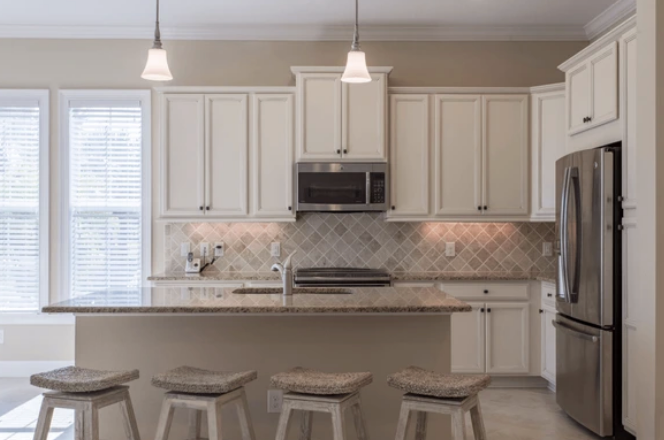 A kitchen with white cabinets and stools and a stainless steel refrigerator