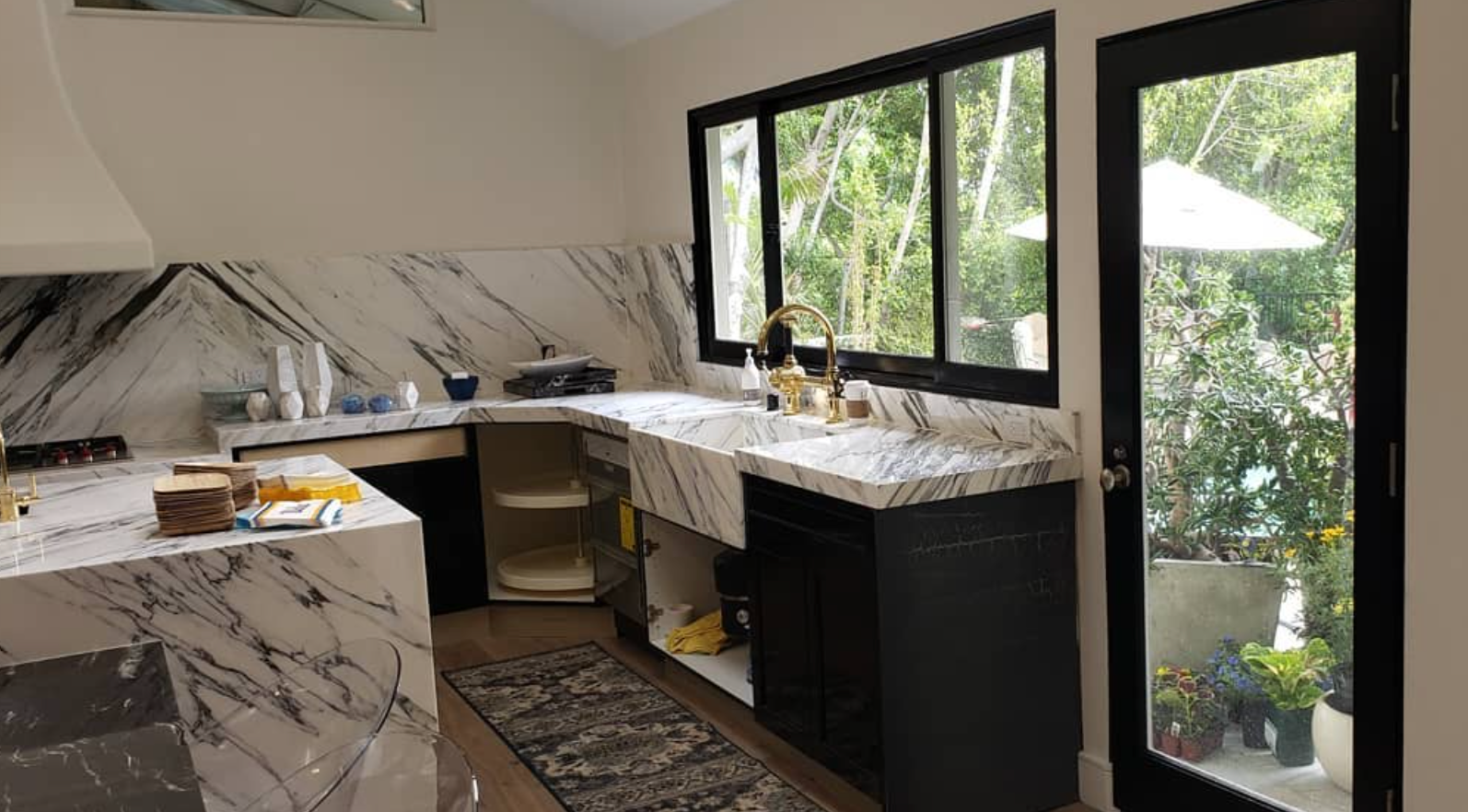 A kitchen with marble counter tops , black cabinets and sliding glass doors.