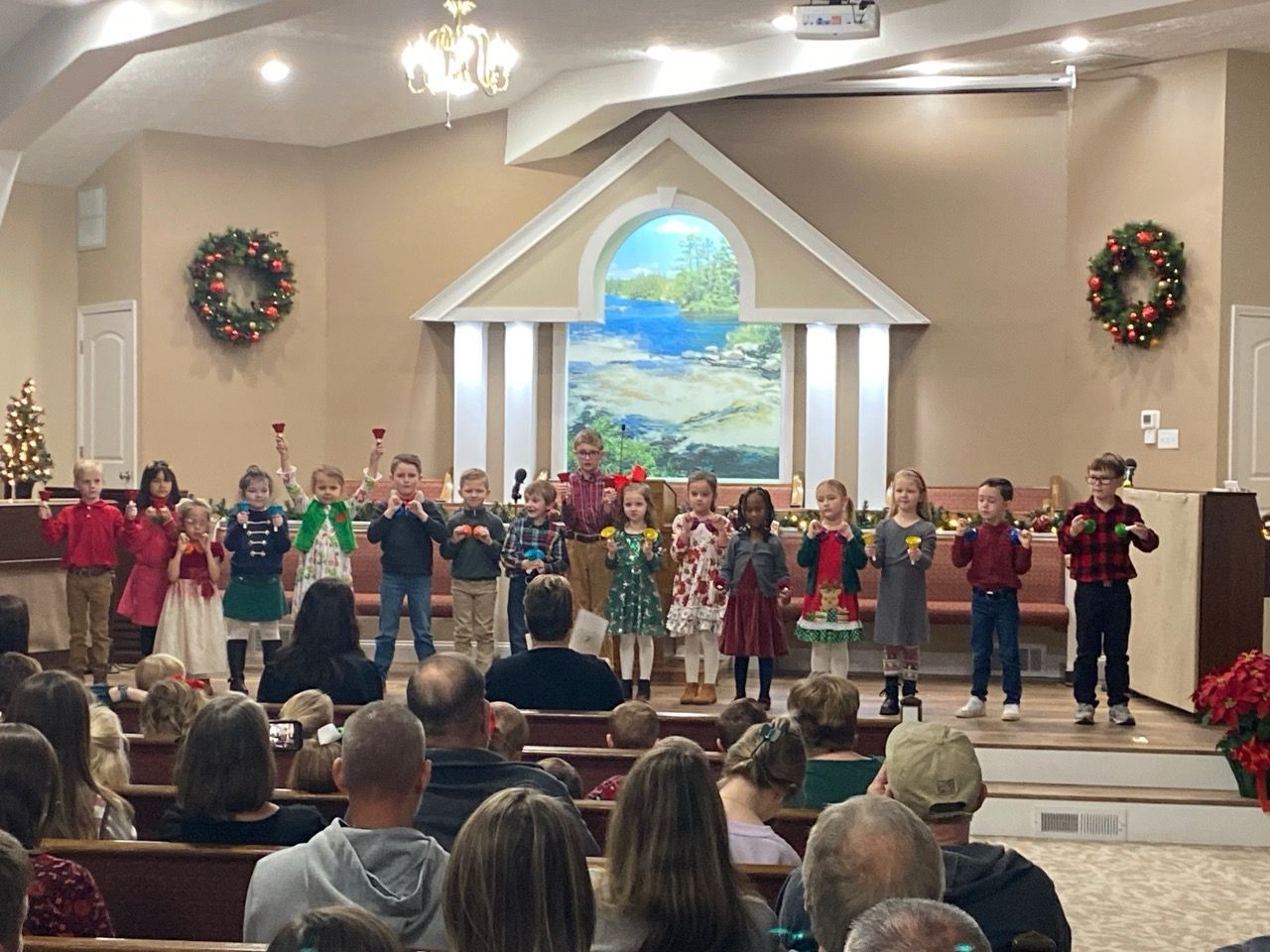 Children performing on a church stage with wreaths and a painted backdrop, viewed from the audience