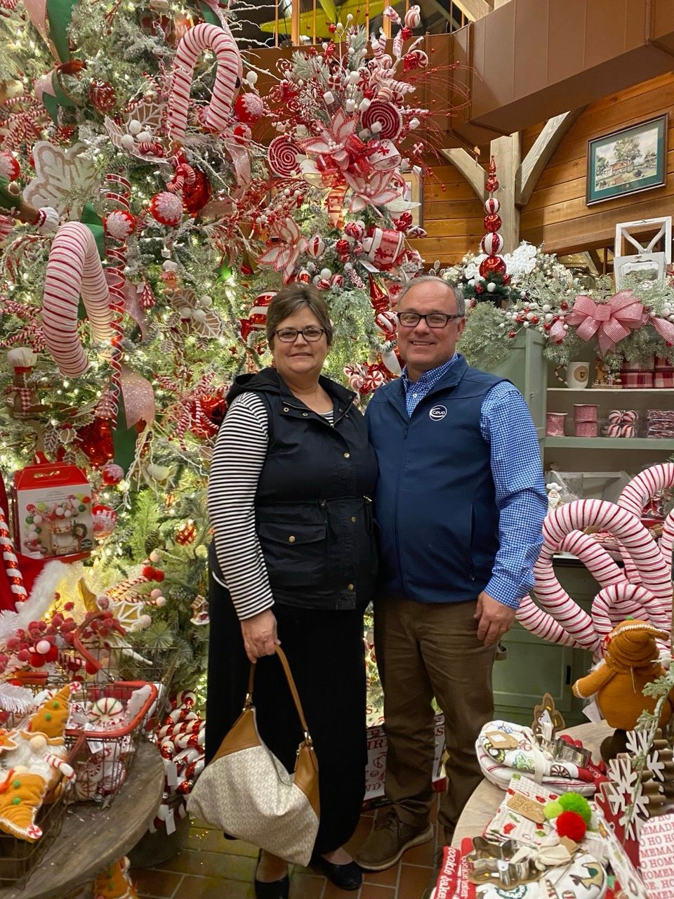Two people posing in a festive holiday display surrounded by pink, red, and white decorations.