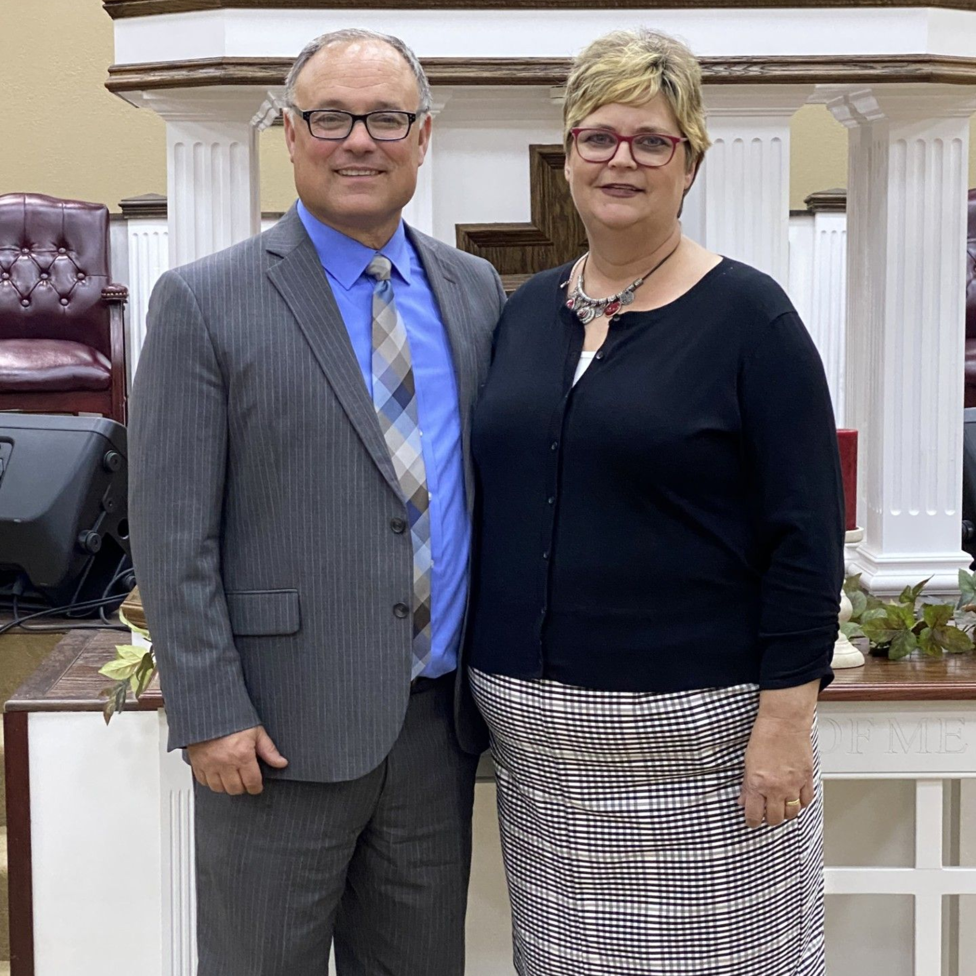 Two people standing together indoors in front of white columns, wearing business attire and smiling.
