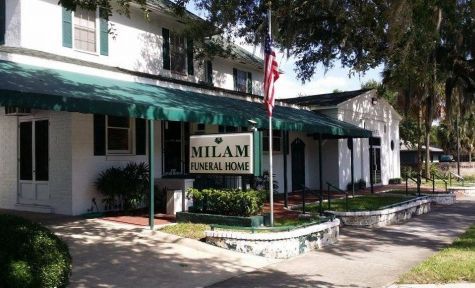 Milam Funeral Home building with green awning and American flag in front yard