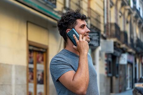 Man in gray T-shirt smiling while talking on a smartphone on a city street