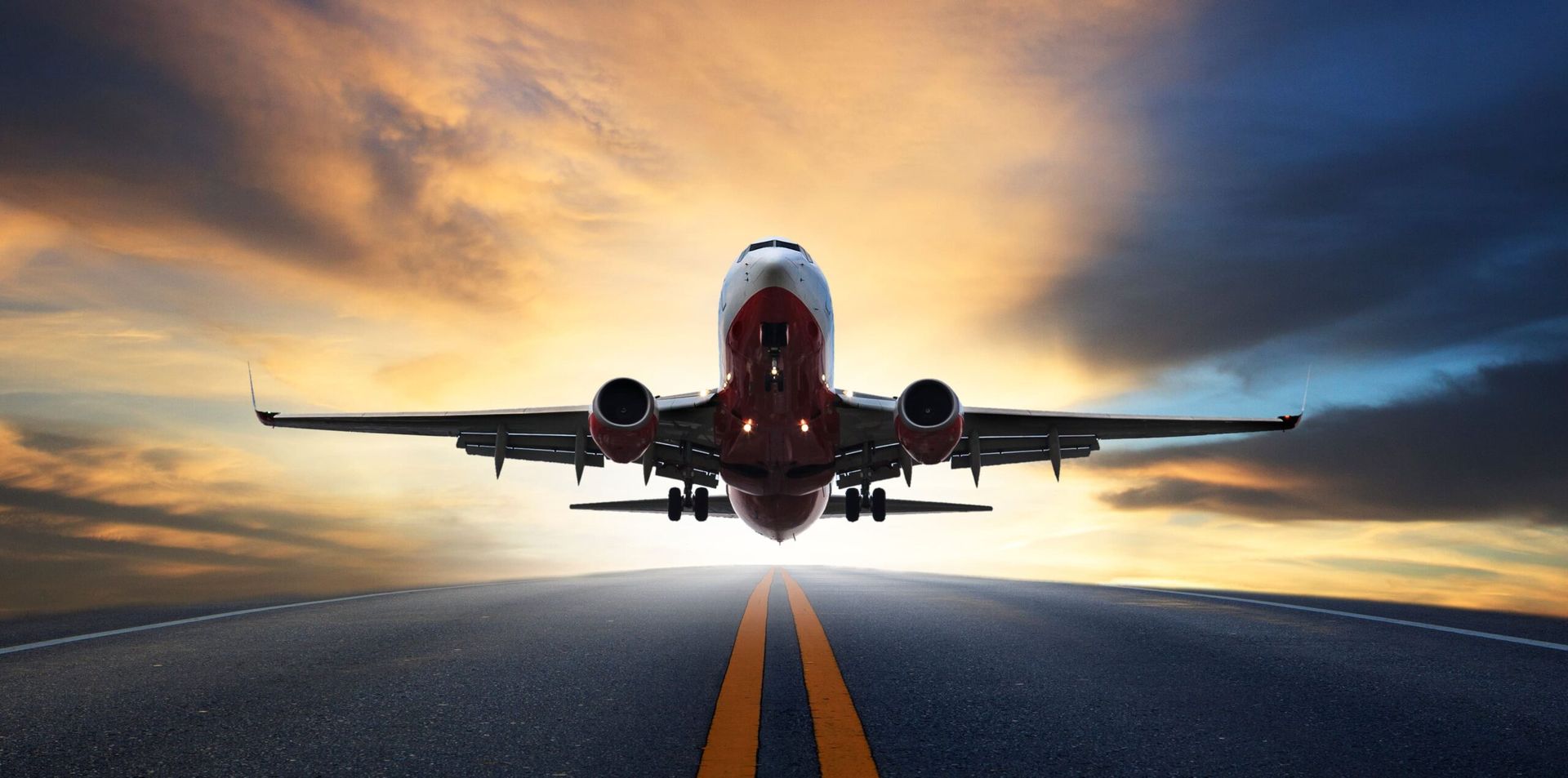 Jet airliner taking off from a runway at sunset, viewed head-on with glowing sky behind it