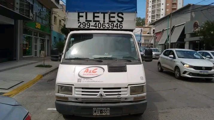 Almacén con palés apilados, cajas envueltas y una pequeña mesa con papeles en un pasillo de almacenamiento.