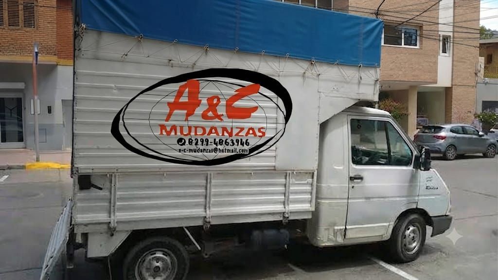Cuatro operarios vestidos de negro desempaquetan cajas en una luminosa sala de estar con suelos de madera.