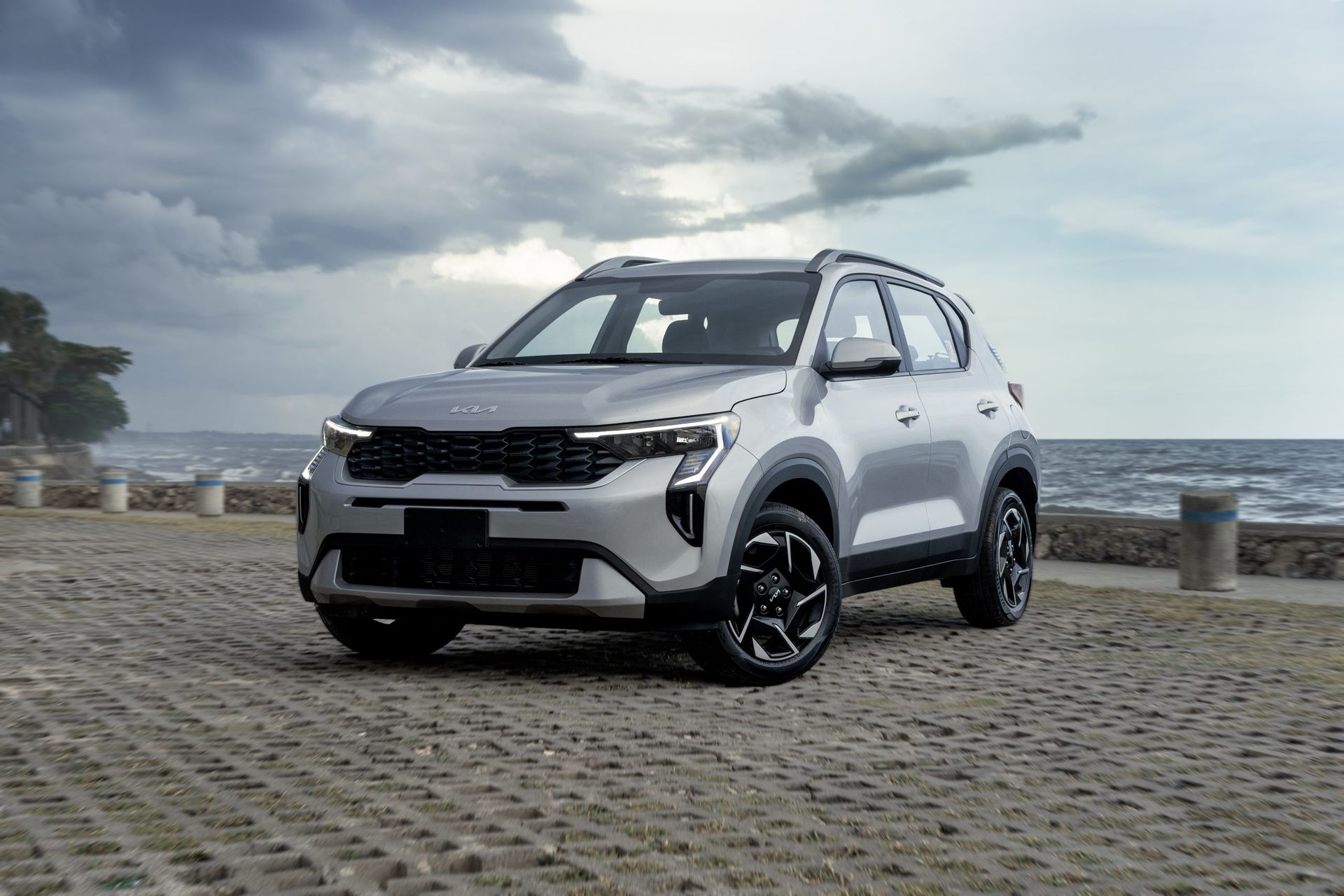 A silver car is parked on a cobblestone road next to the ocean.
